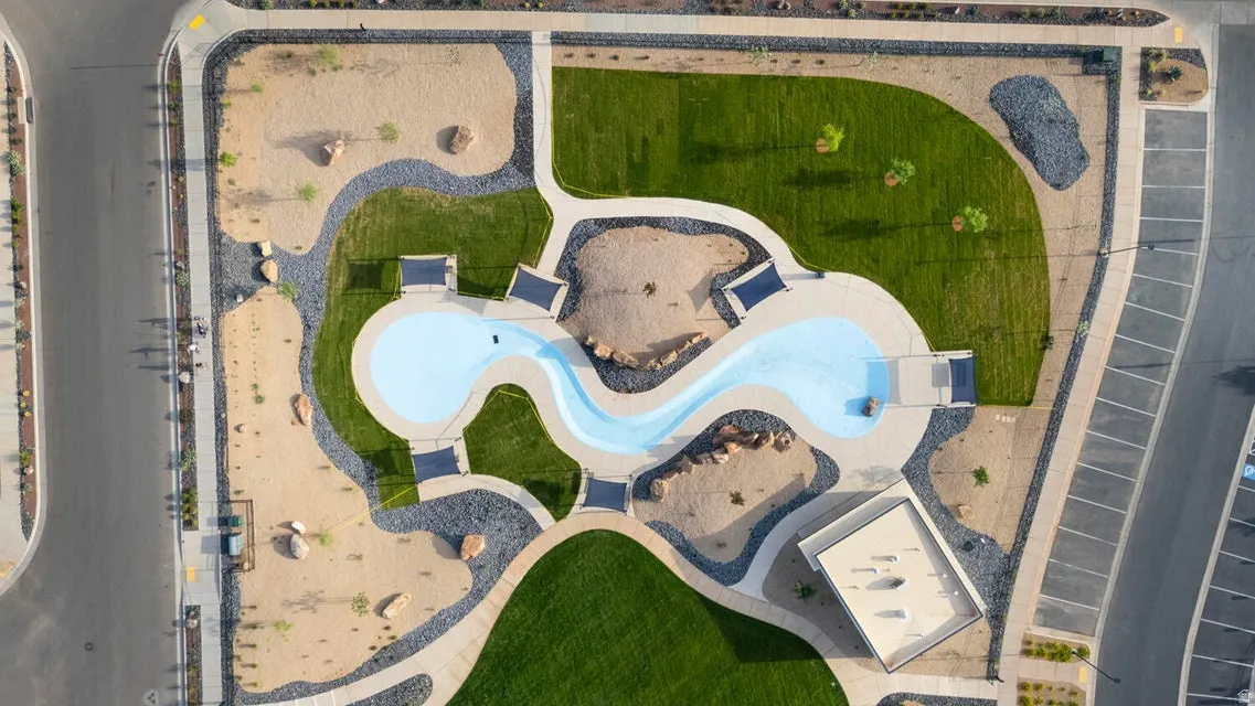 Recreational area featuring a winding water feature, expansive green spaces, surrounding xeriscaping, defined pathways, and overhead shade structures