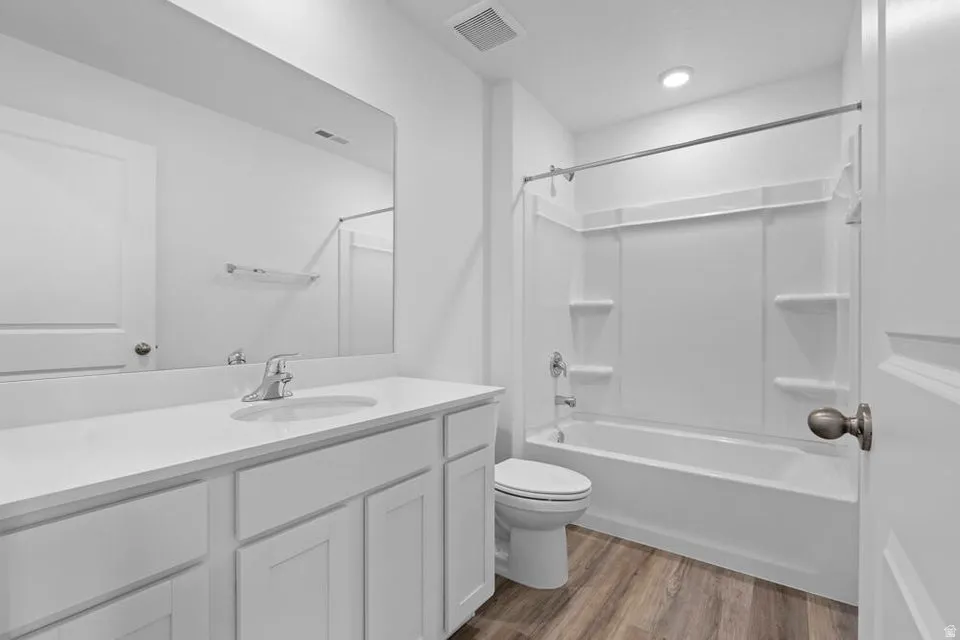 Full bathroom featuring a white vanity with integrated sink, a large wall-mounted mirror, a tub-shower combination with white surround, and wood-finish flooring