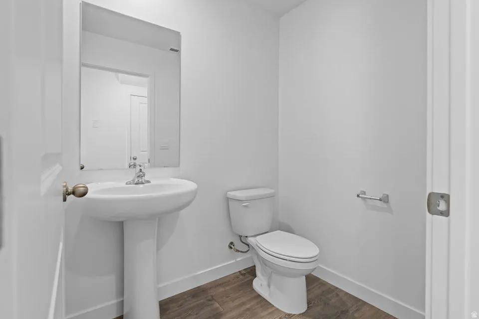 Pedestal sink with chrome faucet, wall-mounted mirror, toilet, and wood-finish flooring
