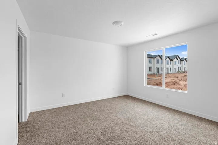 Bright room featuring a large window, neutral carpeting, white walls, and a flush-mount ceiling light