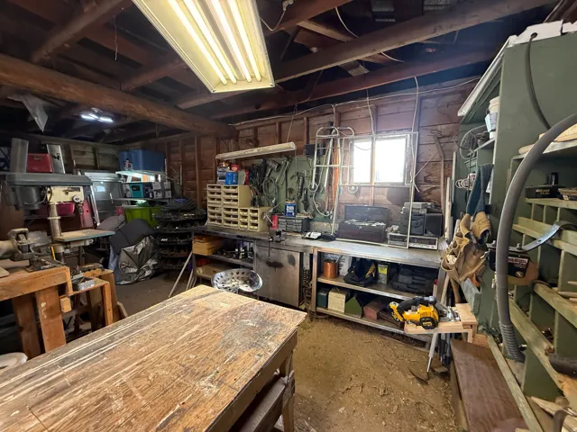 Utility space featuring exposed wood beam ceiling, fluorescent lighting, built-in shelving, a workbench, and a window