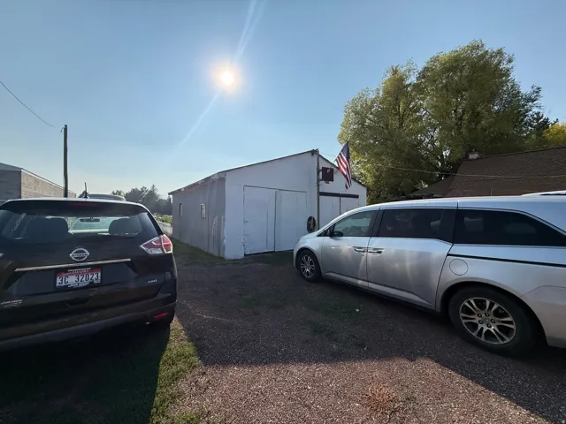 White metal-sided outbuilding with dual barn doors and an attached flag mount