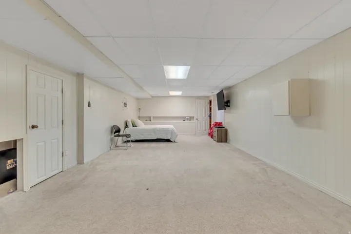 Spacious room featuring light-colored carpeting, white paneled walls, and a dropped ceiling with recessed lighting
