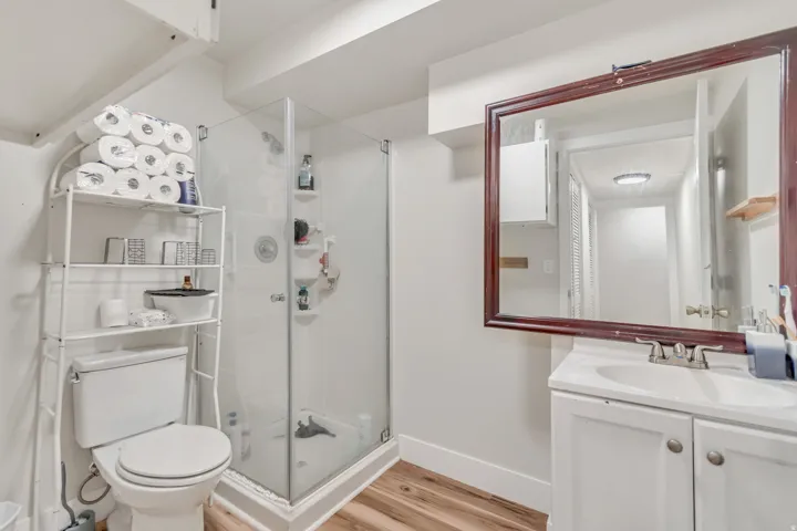 Bathroom featuring wood-finish flooring, a glass-enclosed shower, a vanity with a base cabinet, and a framed mirror