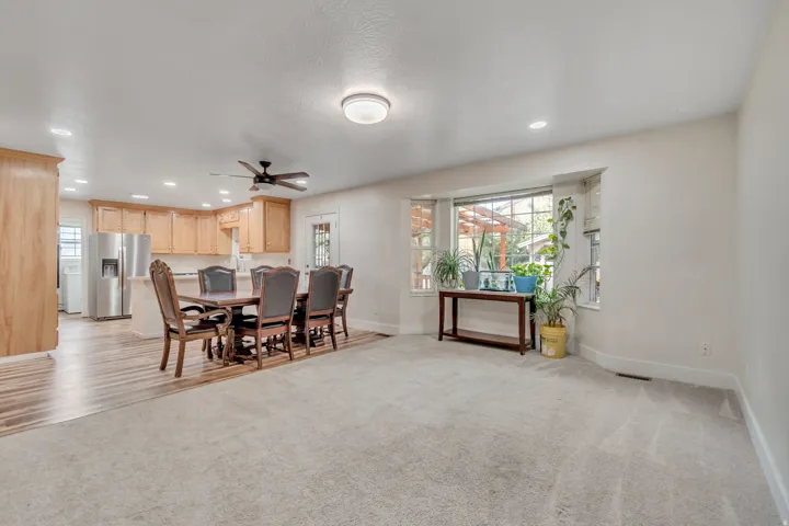 Spacious open-concept living area featuring warm wood-finish cabinetry, stainless steel appliances, ceiling fan with recessed lighting, and plush carpeting throughout
