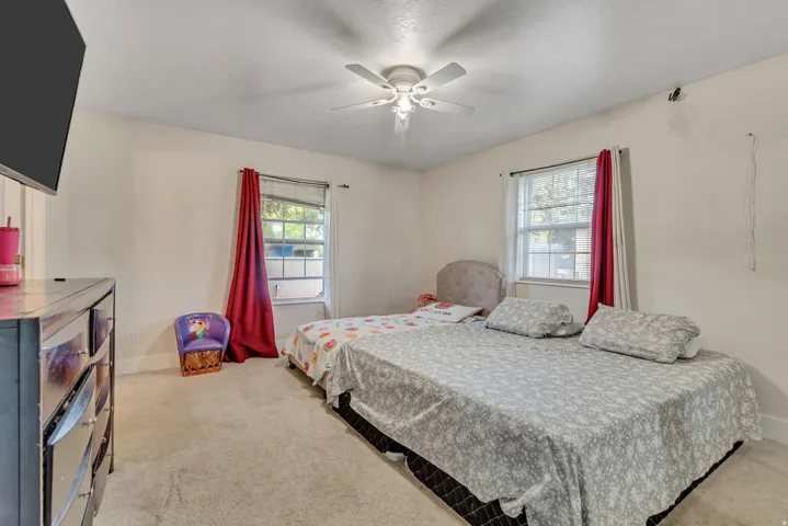 Carpeted bedroom with two windows featuring red drapes