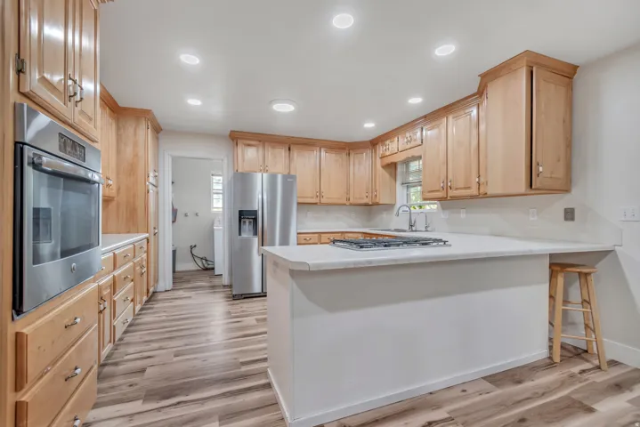 Kitchen featuring light wood cabinetry, stainless steel appliances, wood-finish flooring, white countertops, and recessed lighting