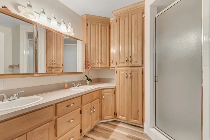 Bathroom featuring a double vanity with light wood cabinetry, a light-colored countertop, and two framed mirrors