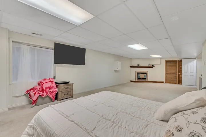 Spacious carpeted room featuring a white drop ceiling with recessed lighting, a mounted television, and a fireplace with a wood mantle