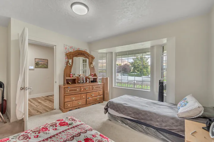 Carpeted interior space featuring a bay window, ceiling-mounted light fixture, and an open doorway revealing wood-finish flooring