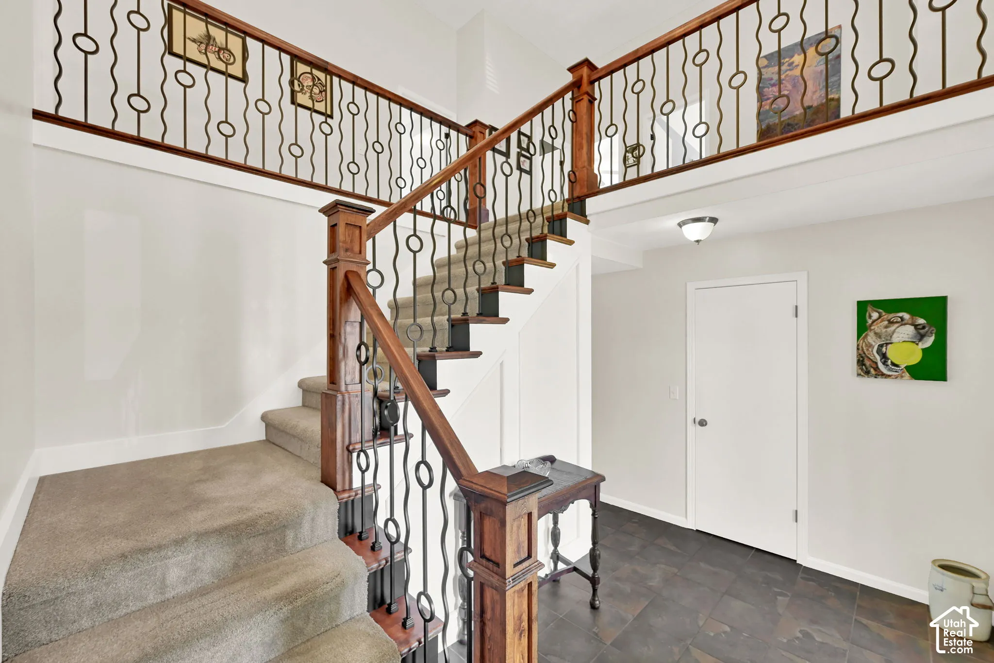 Two-story foyer featuring a carpeted staircase with wood-finish handrails and decorative wrought iron balusters