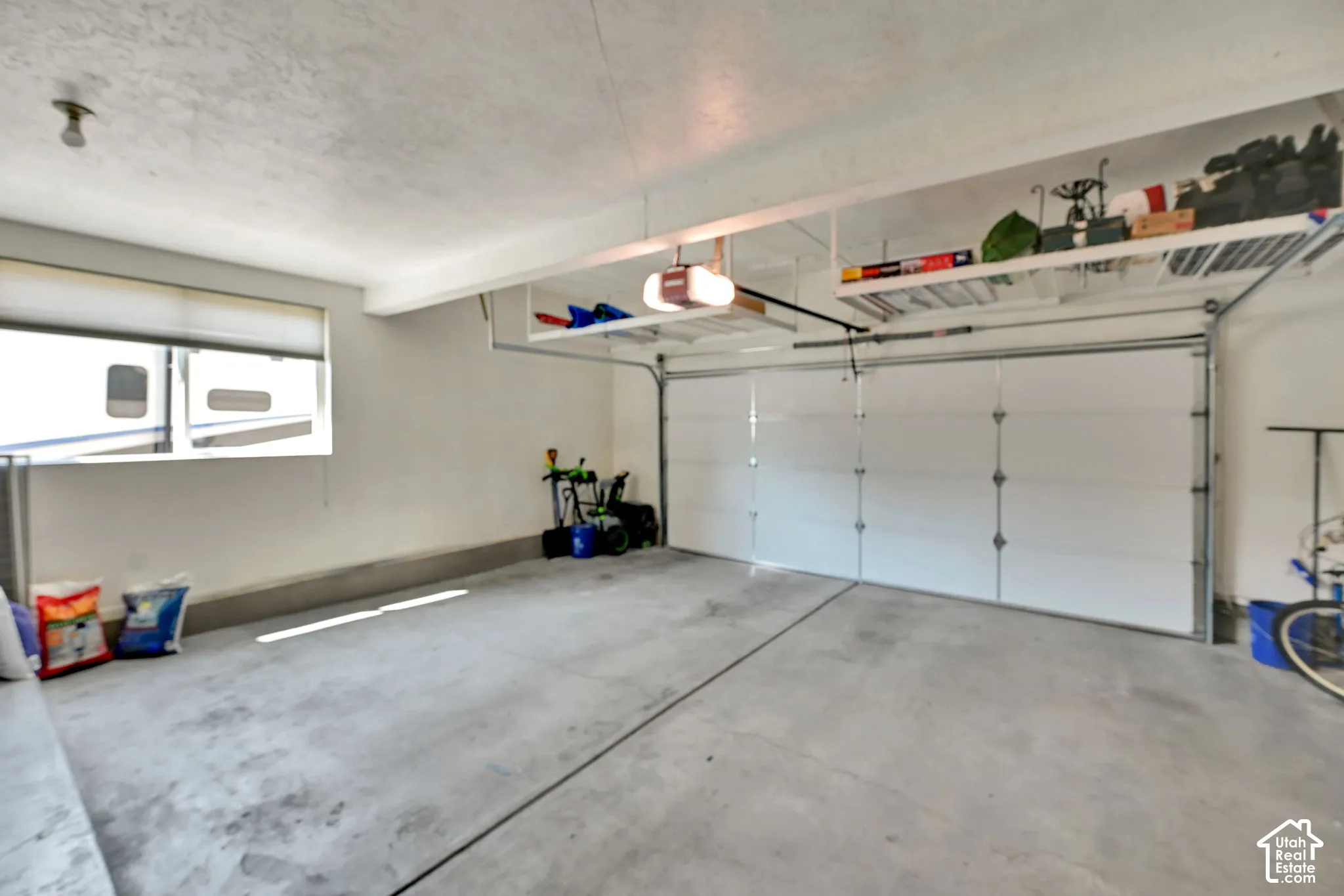 Spacious garage featuring a concrete floor, overhead shelving, a garage door opener, and a large window with a roller shade