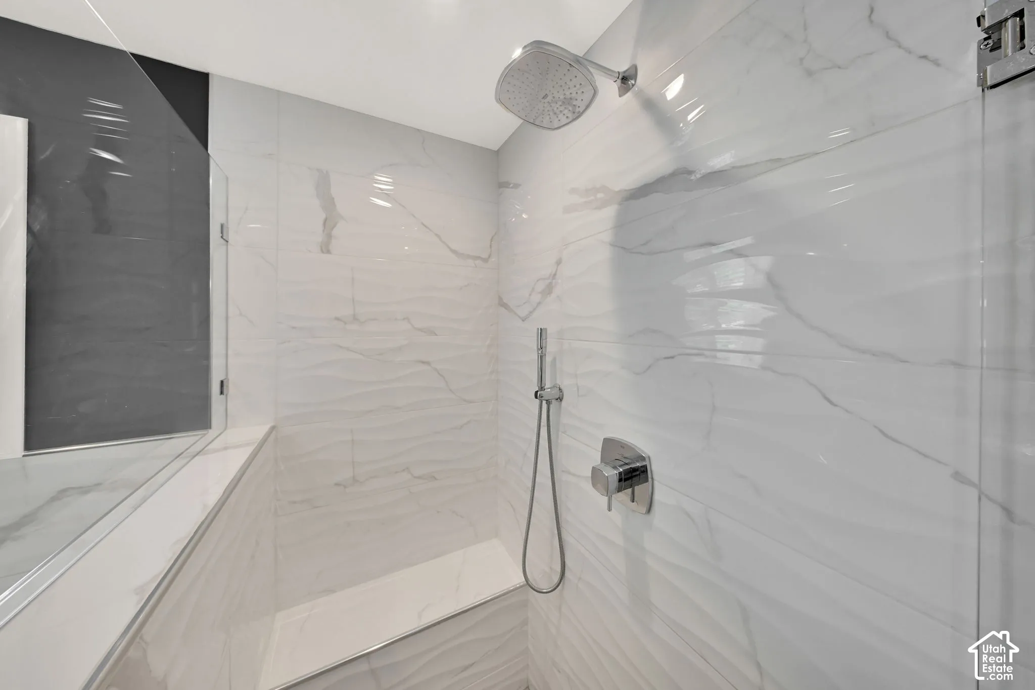 Spa-inspired shower featuring tiled walls, large-format marble-look tile flooring, frameless glass enclosure, rainfall showerhead, and hand-held shower wand with modern chrome fixtures