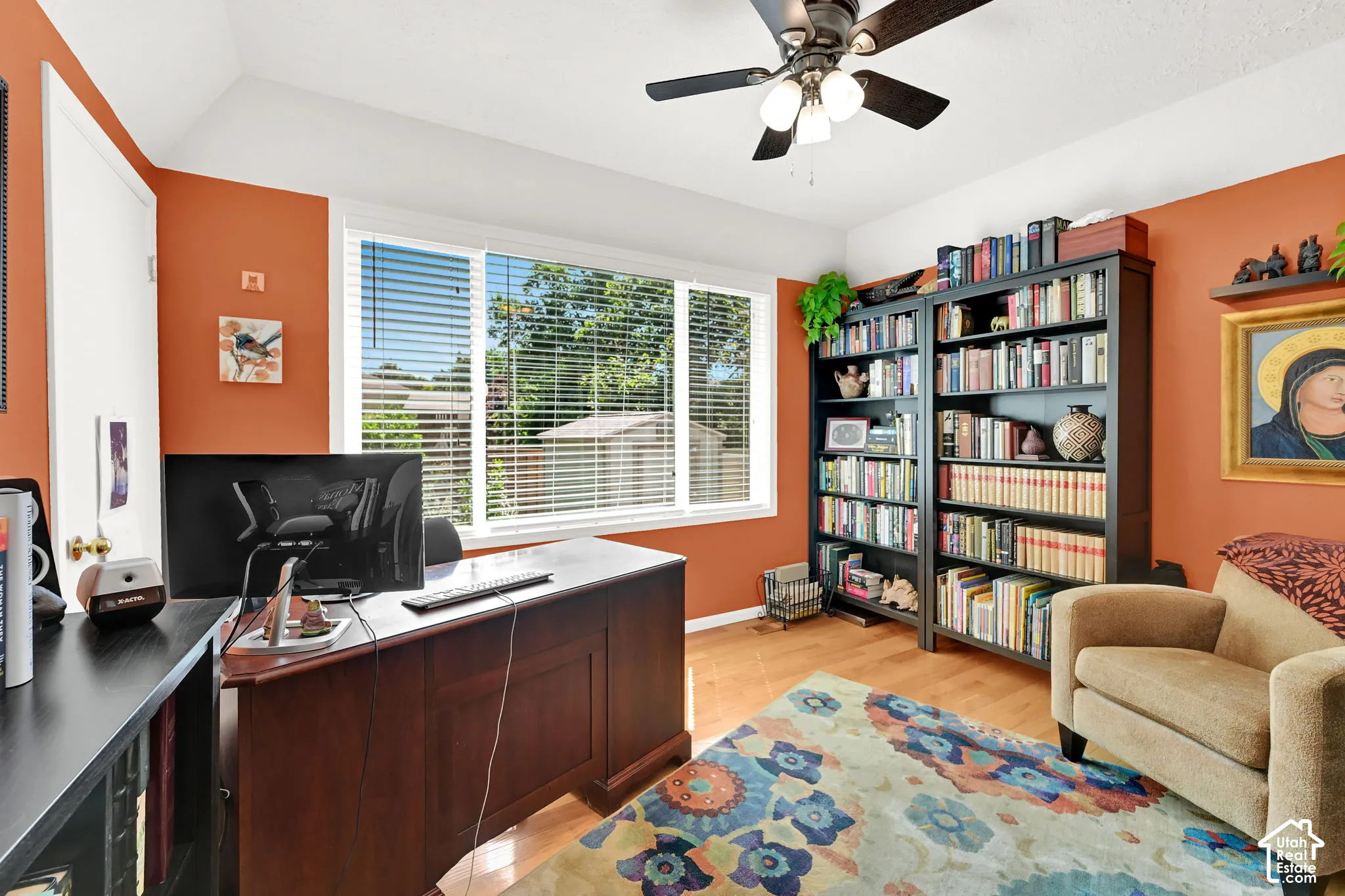 Bright interior room featuring a ceiling fan with integrated lighting, wood-finish flooring, large windows, and vibrant painted walls