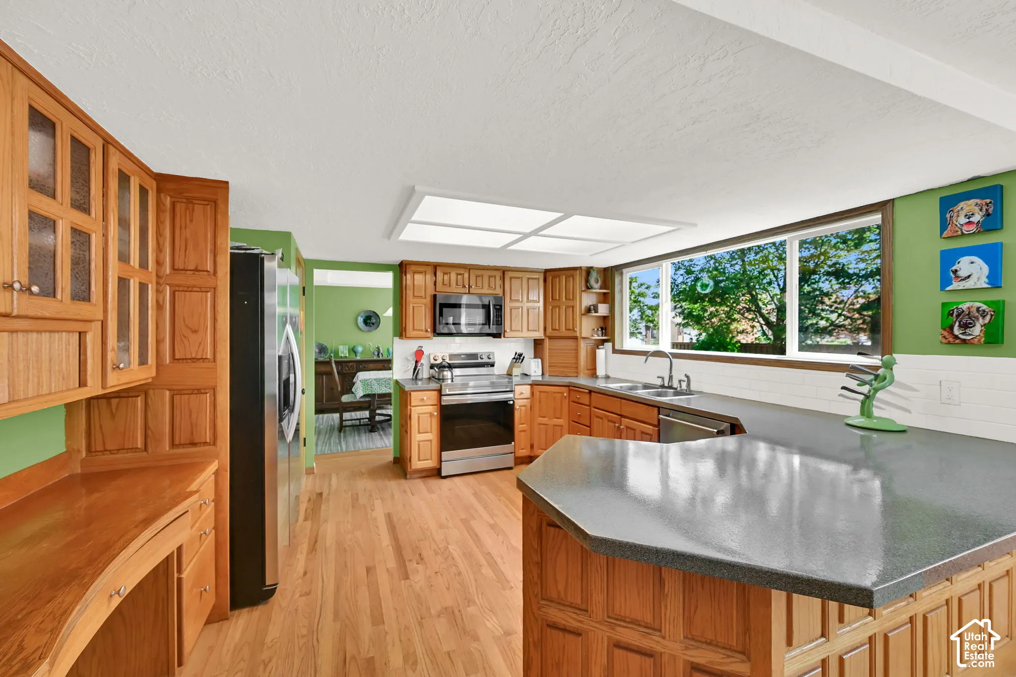 Spacious kitchen featuring warm wood cabinetry throughout, stainless steel appliances, and a large island with gray countertop