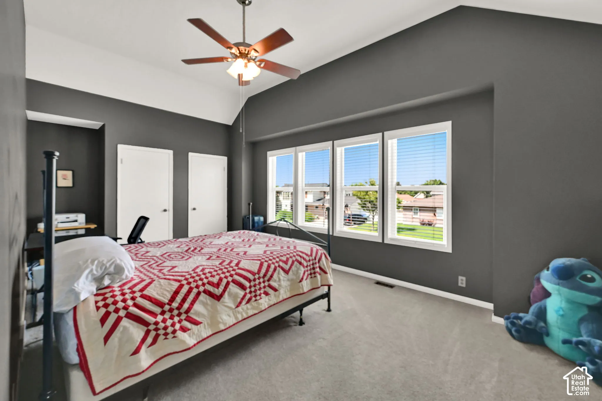Spacious room with vaulted ceilings and a ceiling fan, featuring gray walls and light-colored carpeting