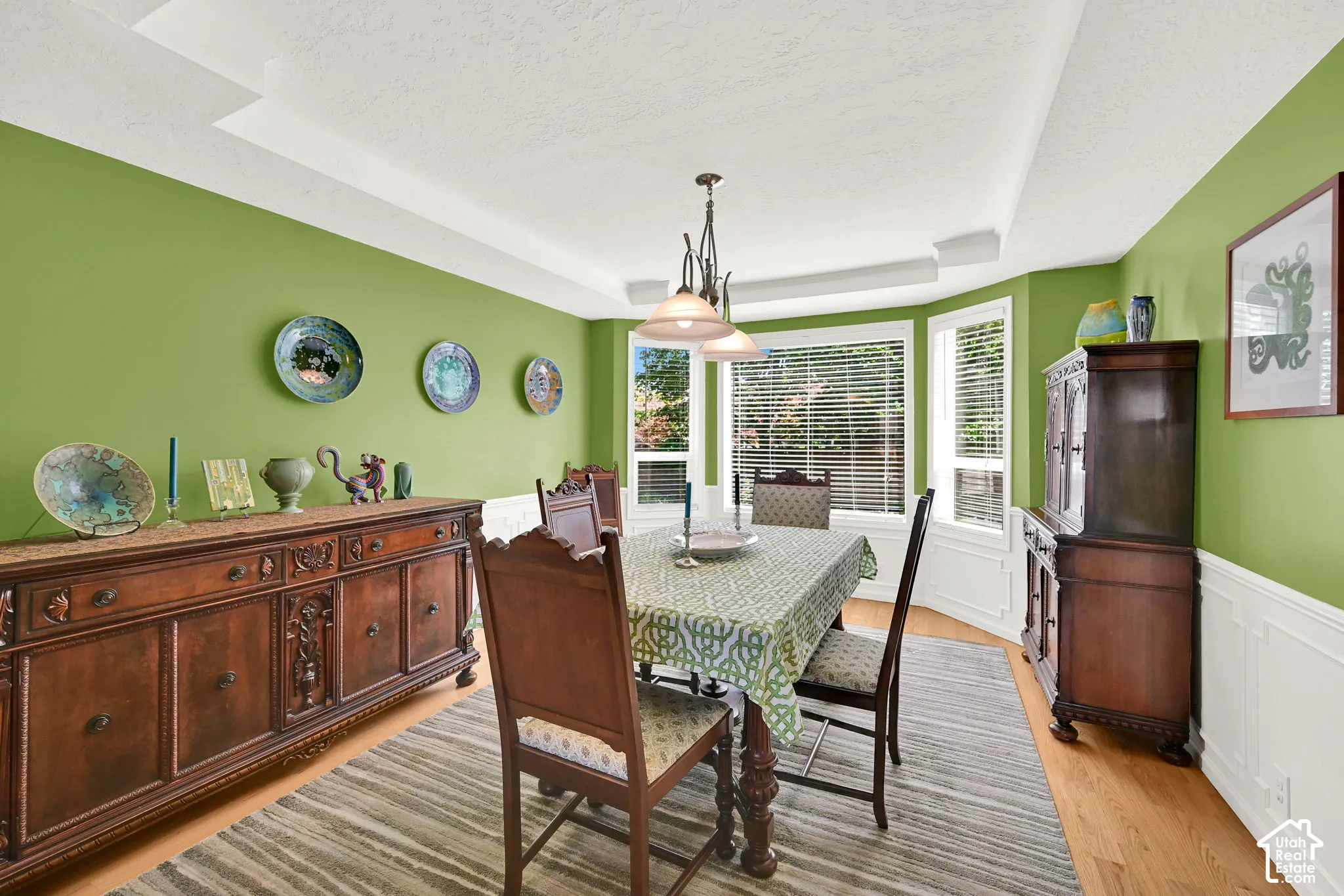 Dining area featuring a bay window, tray ceiling, hardwood flooring, and wainscoting