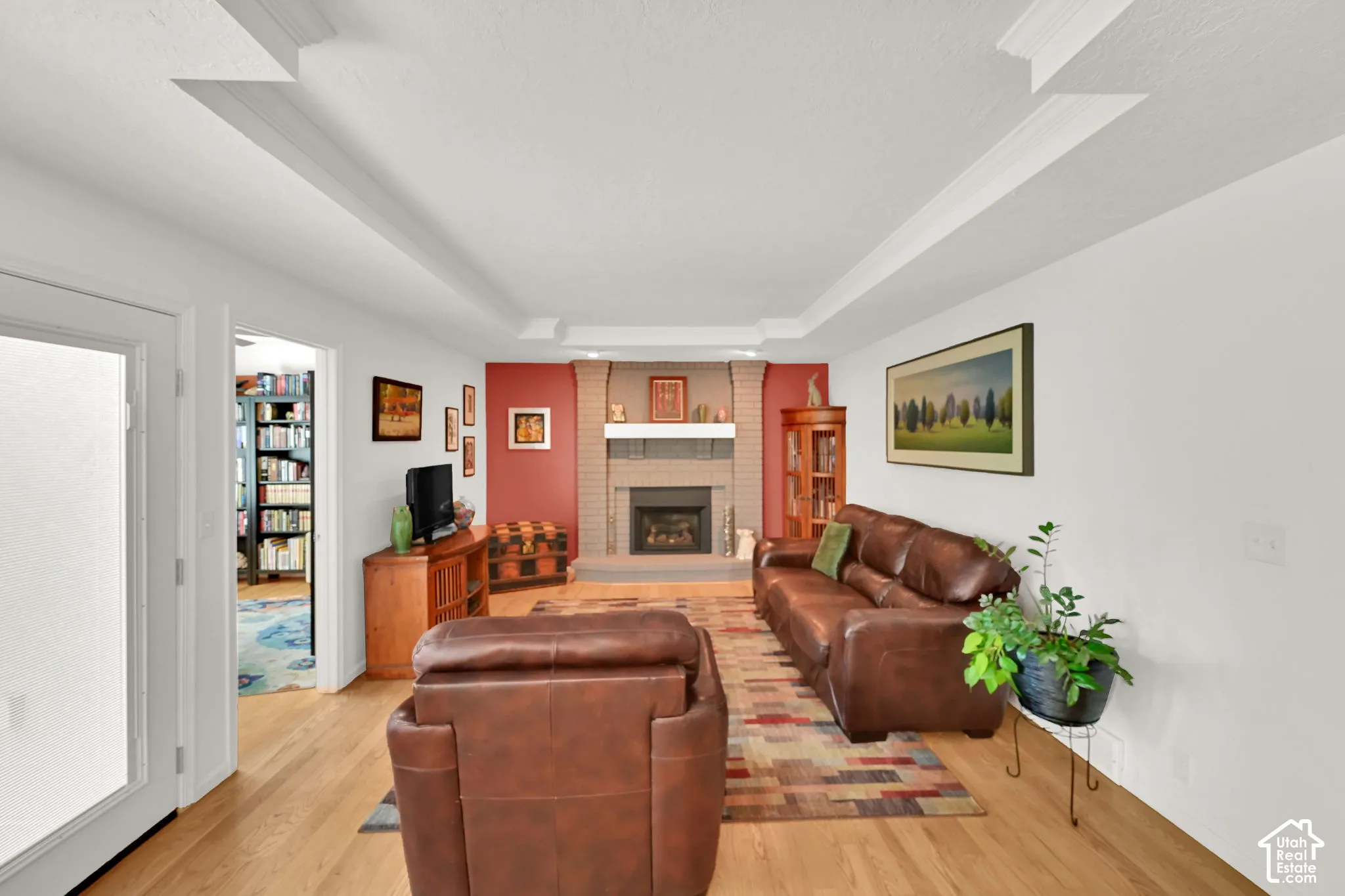 Living room with light wood-finish flooring, a brick fireplace with mantel, and recessed ceiling details