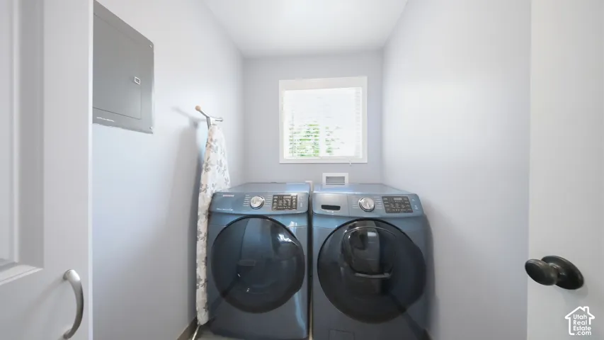 Dedicated laundry room featuring side-by-side front-load washers and dryers with modern stainless-steel finishes, and a window providing natural light