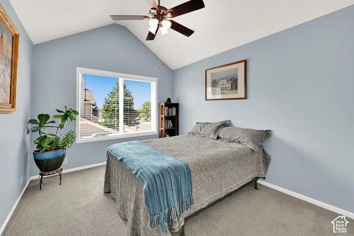 Serene bedroom featuring soft blue walls, vaulted ceiling with ceiling fan, and abundant natural light from a large multi-pane window