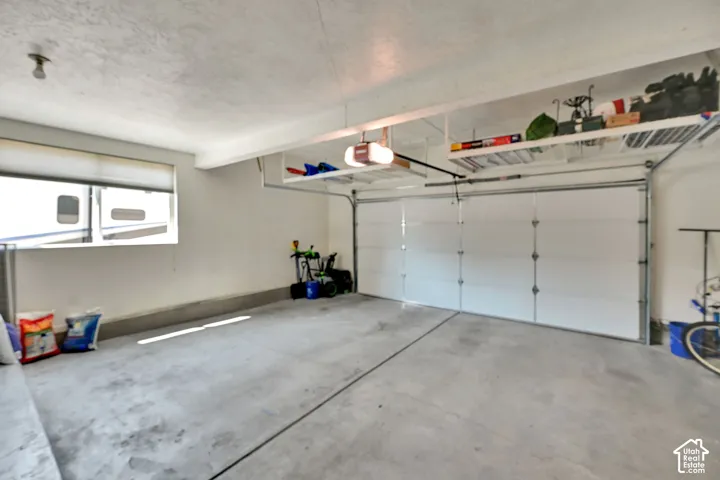 Spacious garage featuring a concrete floor, overhead shelving, a garage door opener, and a large window with a roller shade