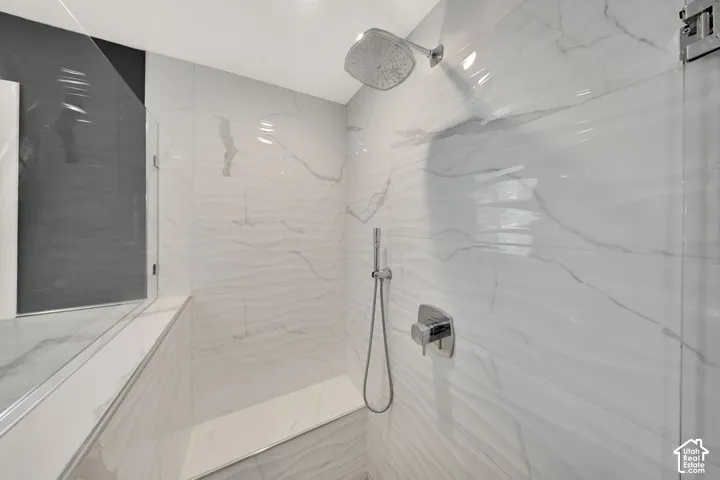 Spa-inspired shower featuring tiled walls, large-format marble-look tile flooring, frameless glass enclosure, rainfall showerhead, and hand-held shower wand with modern chrome fixtures