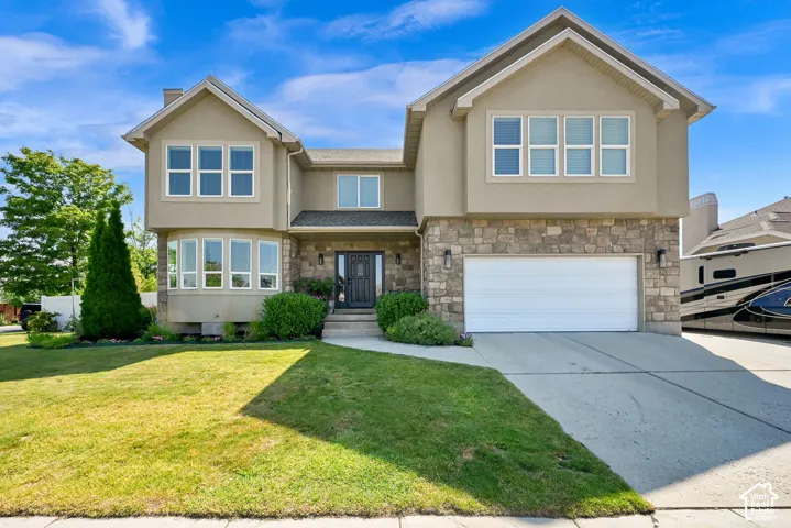 Stucco and stone facade home featuring a two-car garage, bay windows, and a landscaped front yard with a concrete walkway