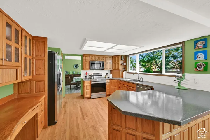 Spacious kitchen featuring warm wood cabinetry throughout, stainless steel appliances, and a large island with gray countertop