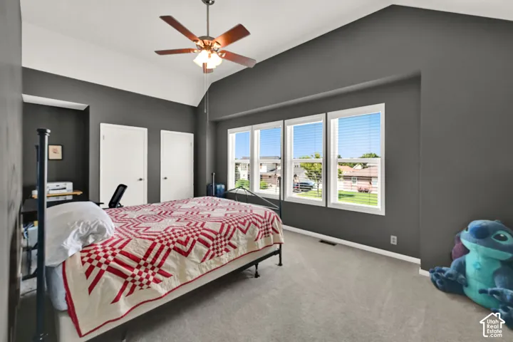 Spacious room with vaulted ceilings and a ceiling fan, featuring gray walls and light-colored carpeting