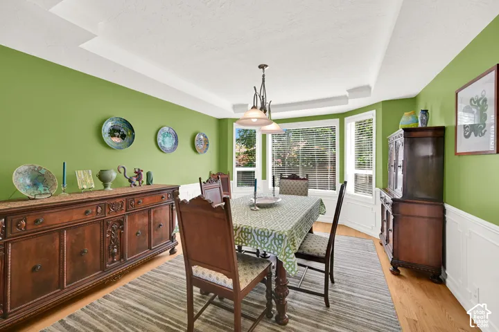 Dining area featuring a bay window, tray ceiling, hardwood flooring, and wainscoting