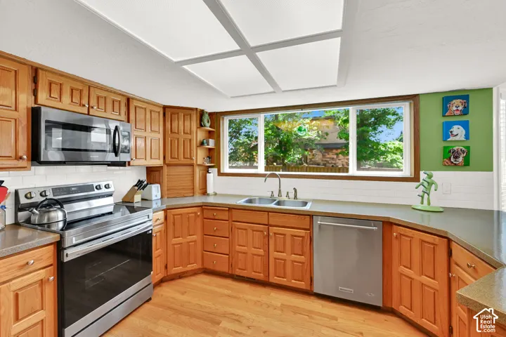 Kitchen featuring honey-toned wood cabinetry, stainless steel appliances, and wood flooring