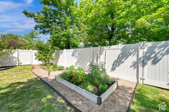 Private backyard oasis featuring a manicured lawn, raised planter beds, mature landscaping, and shade trees providing natural screening and cooling