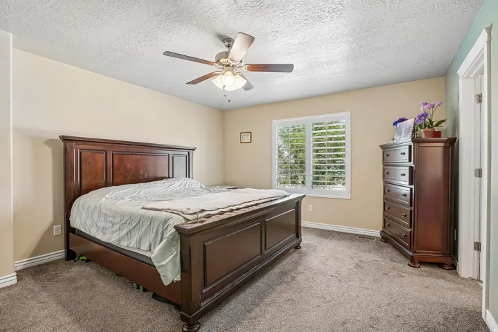 Spacious primary bedroom featuring a wood-frame bed, neutral carpet flooring, and soft cream-colored walls