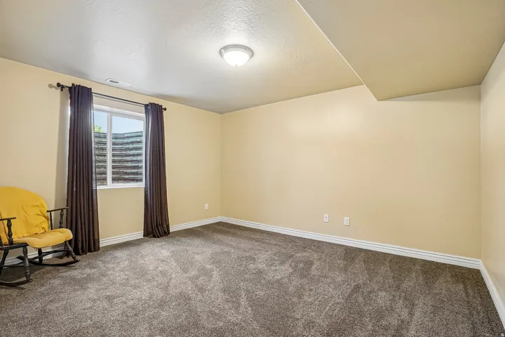 Carpeted room featuring a window with a window well, light cream walls, white trim, and a flush mount ceiling light fixture