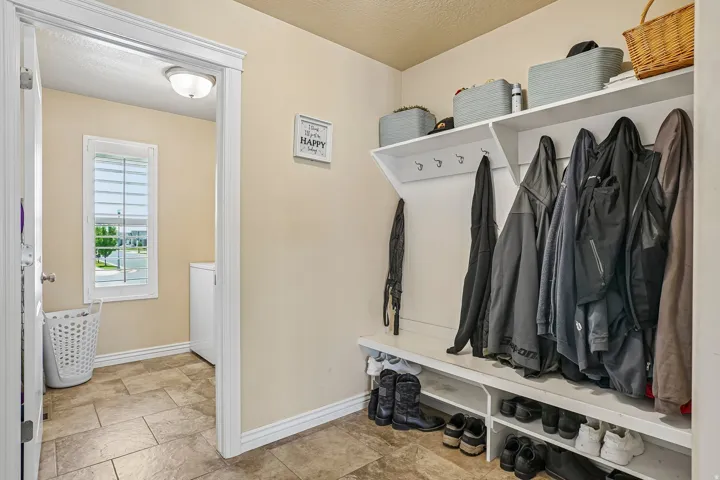 Dedicated mudroom featuring built-in shelving with hooks for organized storage, tile flooring, and abundant natural light from the entry door