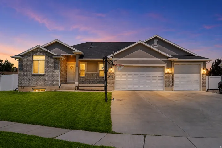 Brick and stucco exterior with an attached three-car garage, concrete driveway, and a front lawn