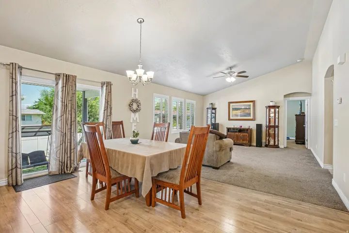 Vaulted ceilings extend over a dining area with wood-finish flooring and a chandelier, opening to a carpeted living space