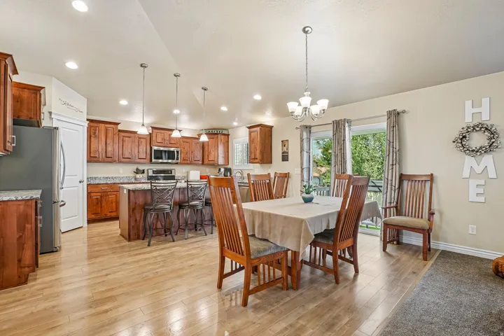 Open-concept kitchen and dining area featuring warm wood-finish cabinetry, stainless steel appliances, recessed and pendant lighting, wood-finish flooring throughout, and a spacious dining zone with seating for multiple guests