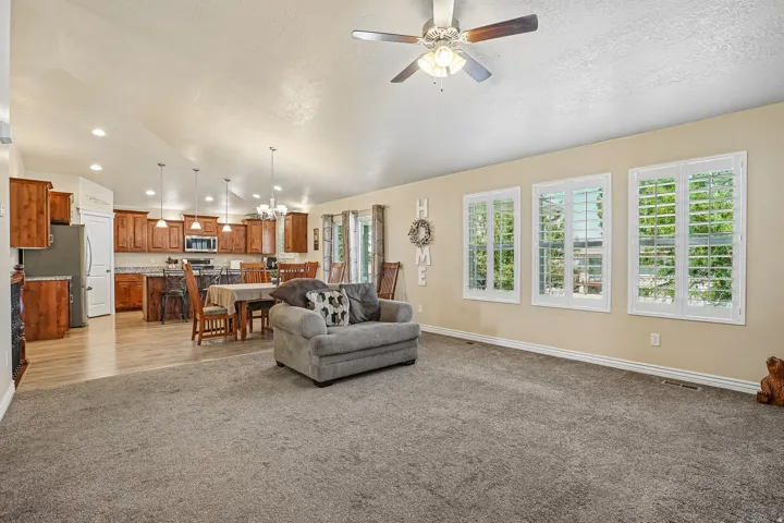 Open-concept living and kitchen area featuring warm wood cabinetry, stainless steel appliances, and abundant natural light from multiple French doors and shuttered windows