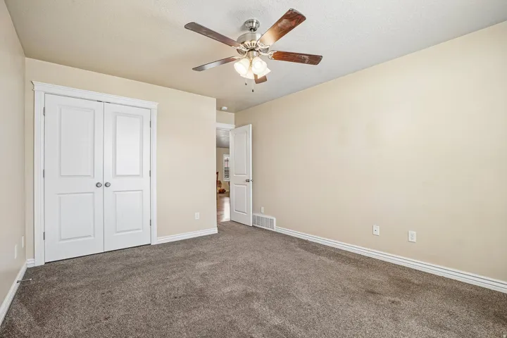 Carpeted interior space featuring a ceiling fan with light fixture, double-door closet, and baseboard trim