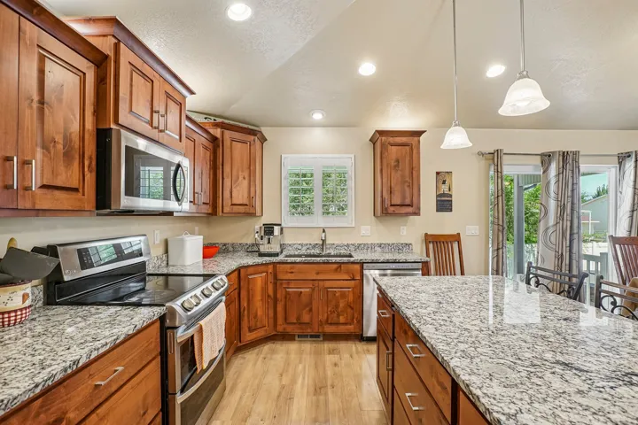 Chef's kitchen showcasing warm wood cabinetry, speckled granite countertops, and stainless steel appliances including a gas range
