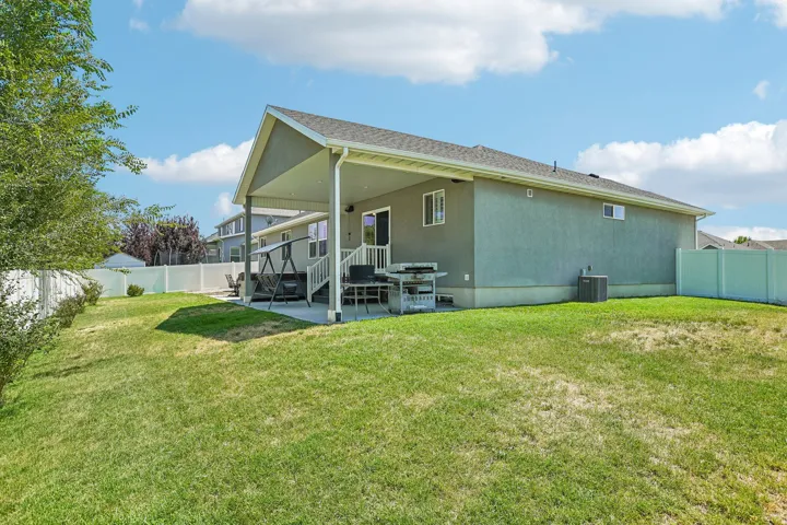 Expansive backyard featuring a covered concrete patio, a slider door entry, and a white privacy fence