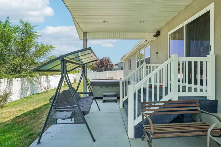 Covered patio with concrete flooring and overhead pergola structure, featuring direct access to the residence via white railing staircase