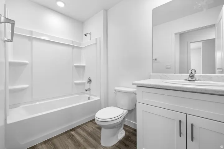 Bathroom featuring a white vanity with an integrated sink, a rectangular mirror, a white toilet, and a bathtub with an integrated shower and shelving