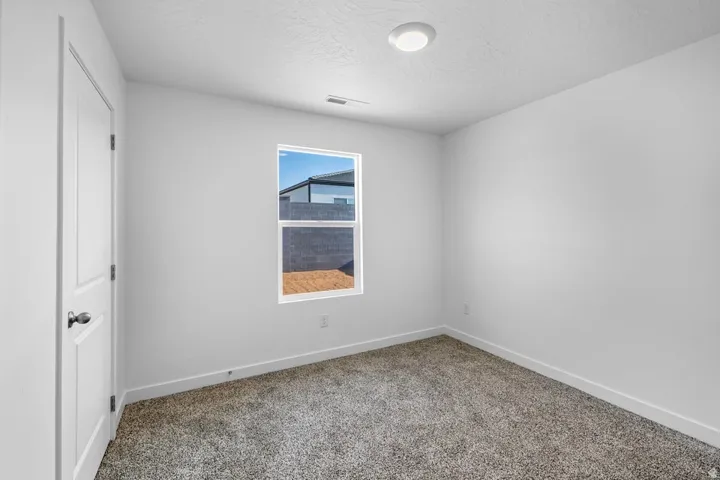 Interior room featuring white walls, textured carpeting, and a window with a black frame