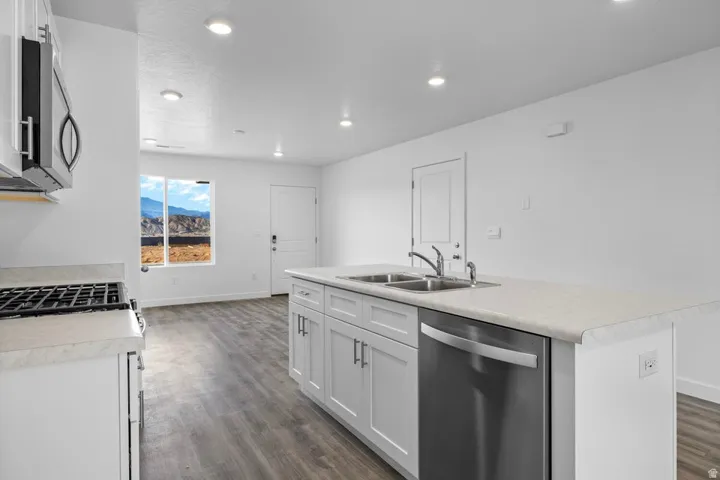 Open-concept kitchen featuring an island with double sinks, stainless steel dishwasher, white cabinetry, light-toned countertops, and wood-finish flooring