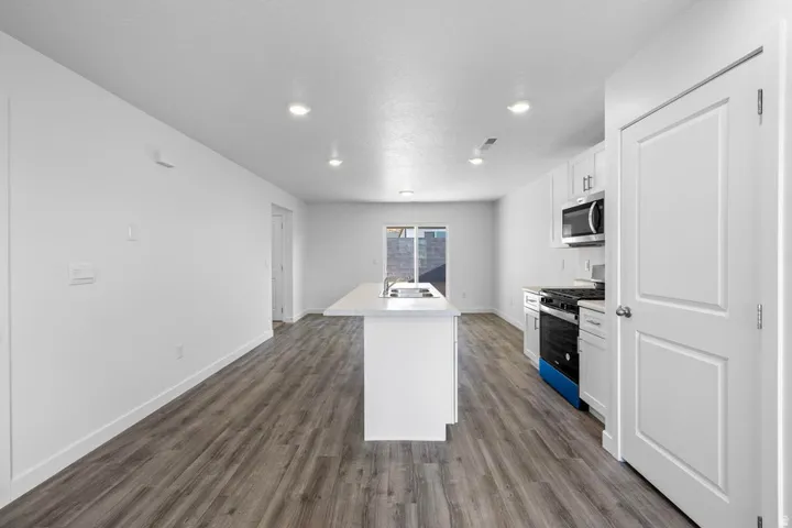 Open-concept kitchen and living area featuring wood-finish flooring, recessed lighting, a kitchen island with sink, white cabinetry, and stainless steel appliances