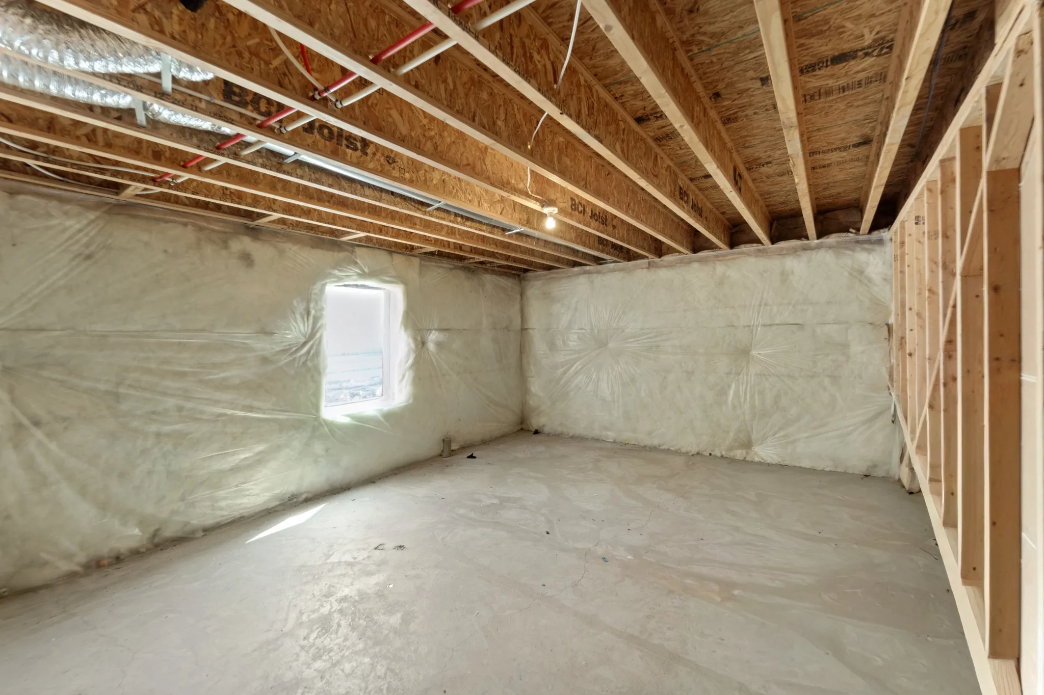 Unfinished basement featuring exposed wood joists, concrete flooring, insulated walls, an egress window, and visible plumbing and HVAC ductwork