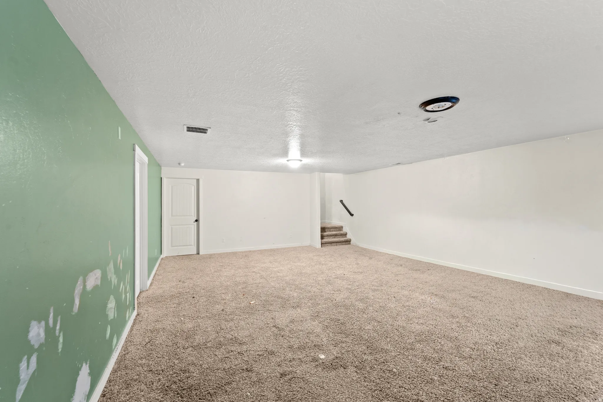 Spacious room with light brown carpet flooring, white walls, and a contrasting green accent wall