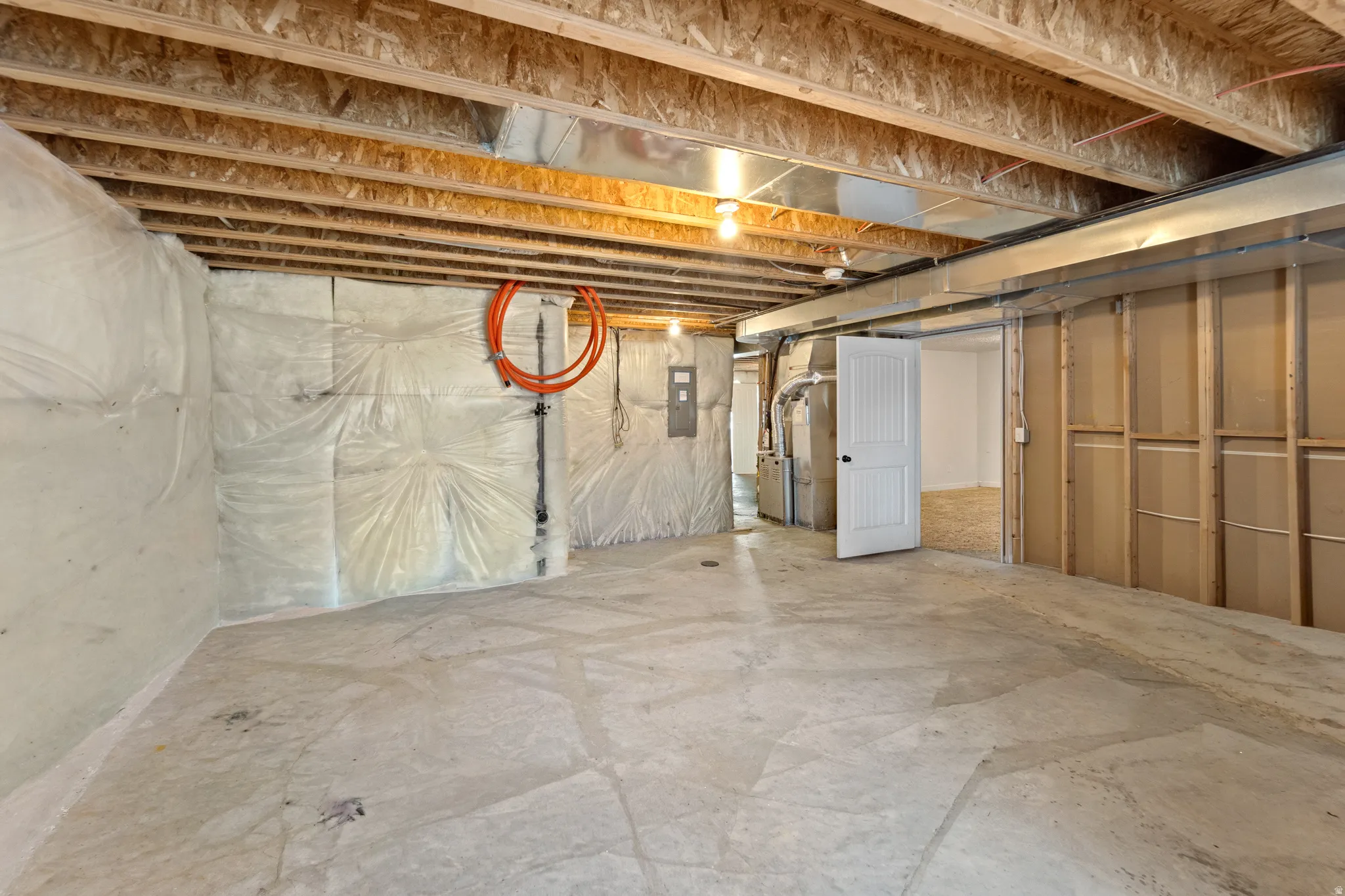 Unfinished basement space featuring exposed wood joists, concrete flooring, and insulated walls